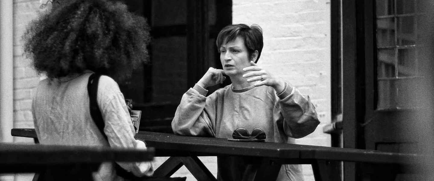 Two women, talking, sitting, picnic bench.