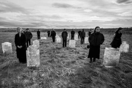 People, dressed in black, standing in a cemetery